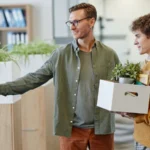Manager welcoming new employee carrying box of belongings in office
