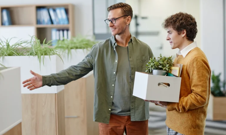 Manager welcoming new employee carrying box of belongings in office